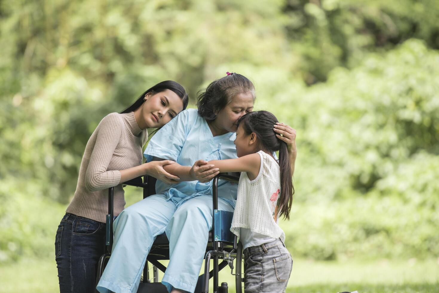 glad mormor i rullstol med sin dotter och barnbarn i en park, lyckligt liv lycklig tid. foto