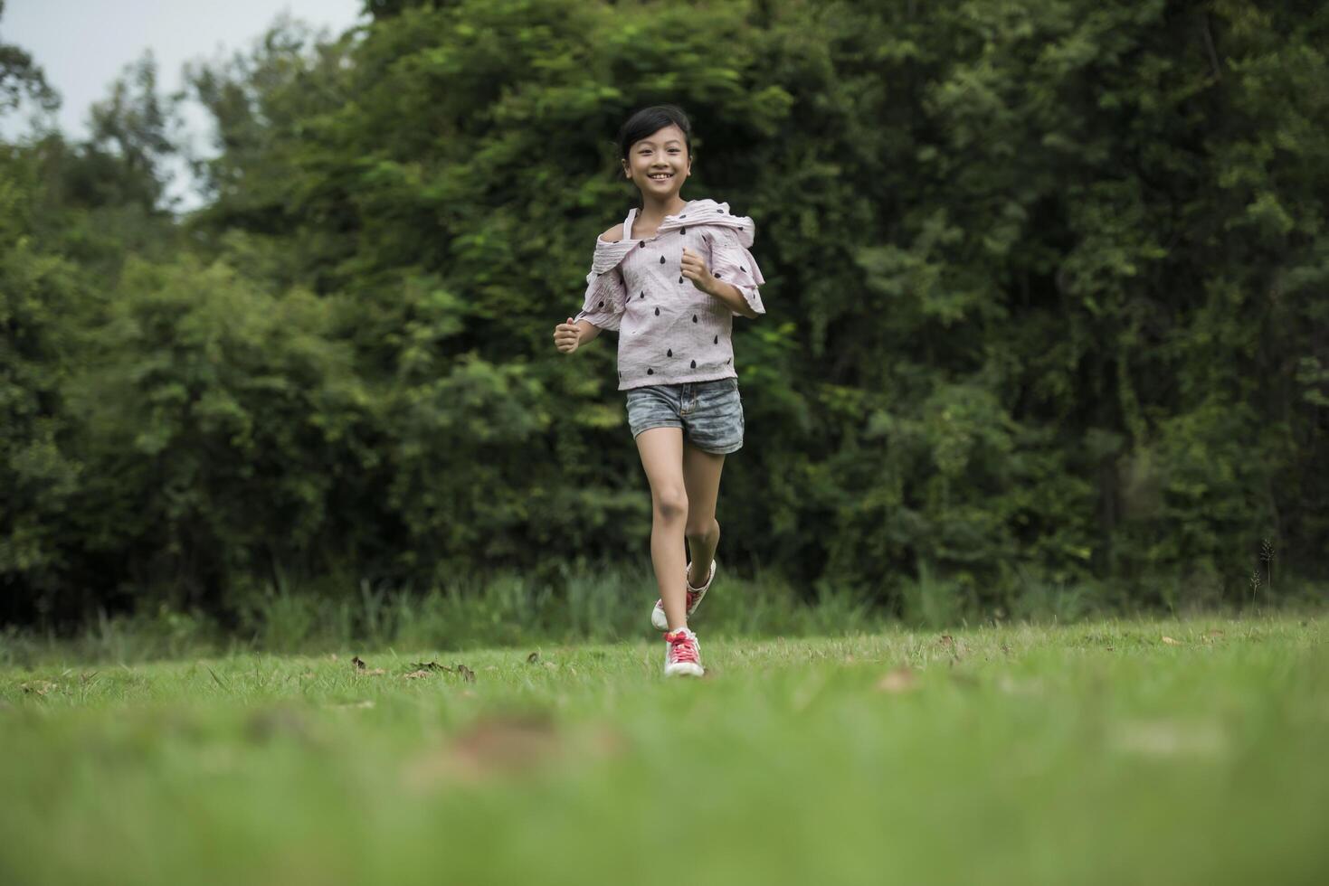 glad söt liten flicka som springer på gräset i parken foto