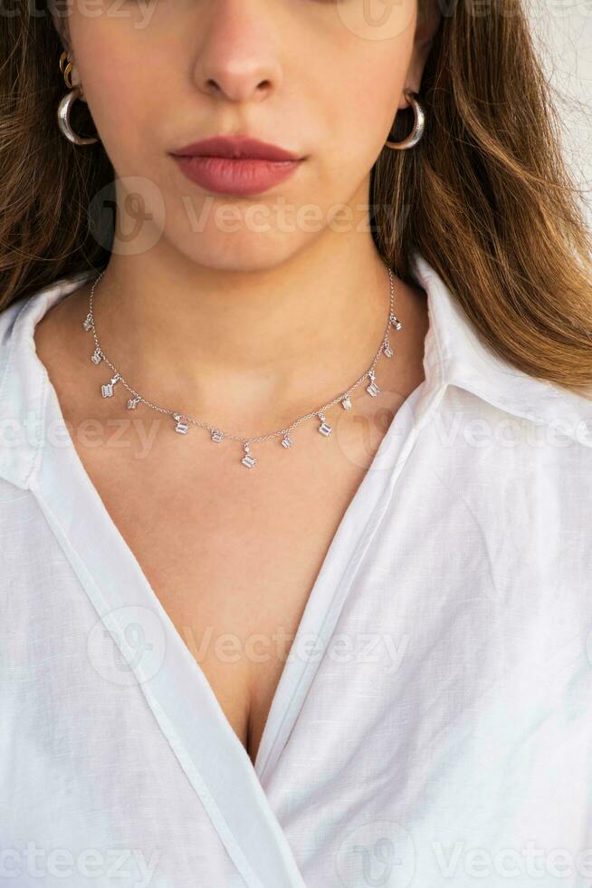 ung kvinna bär en silver- klar halsband och silver- örhängen. foto