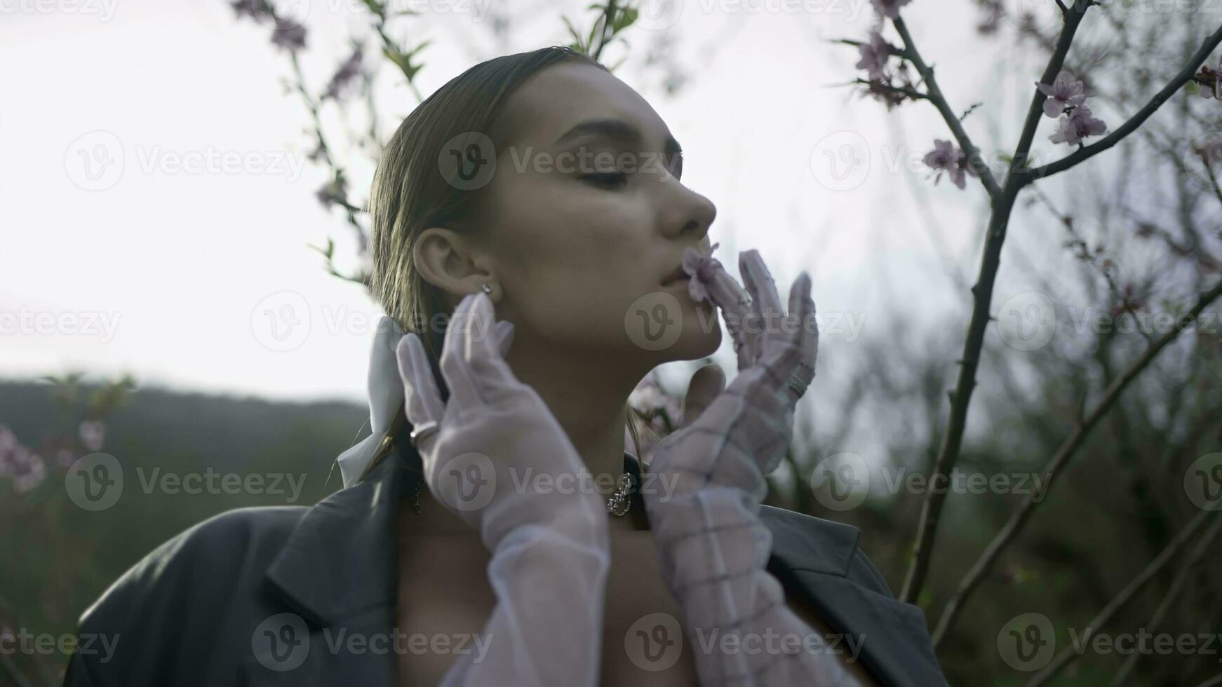 skön kvinna Framställ med blomma förbi träd. handling. eleganta kvinna med blomma från blommande grenar av träd. skön kvinna Framställ med blomma i natur foto