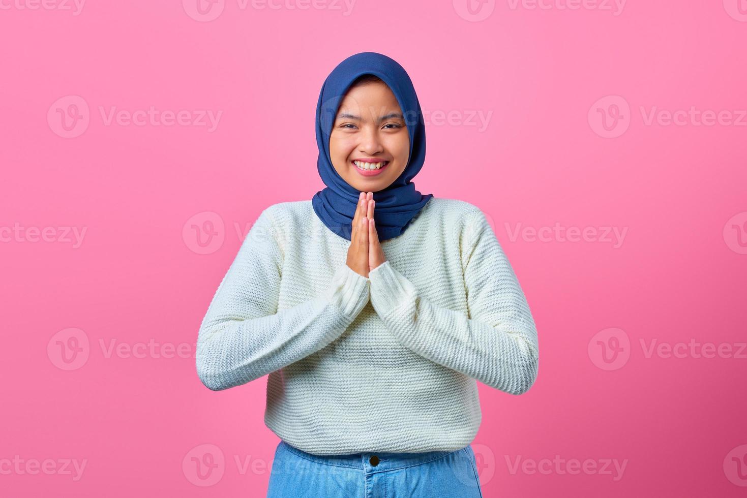 porträtt av leende ung asiatisk kvinna som visar be gest på rosa bakgrund foto