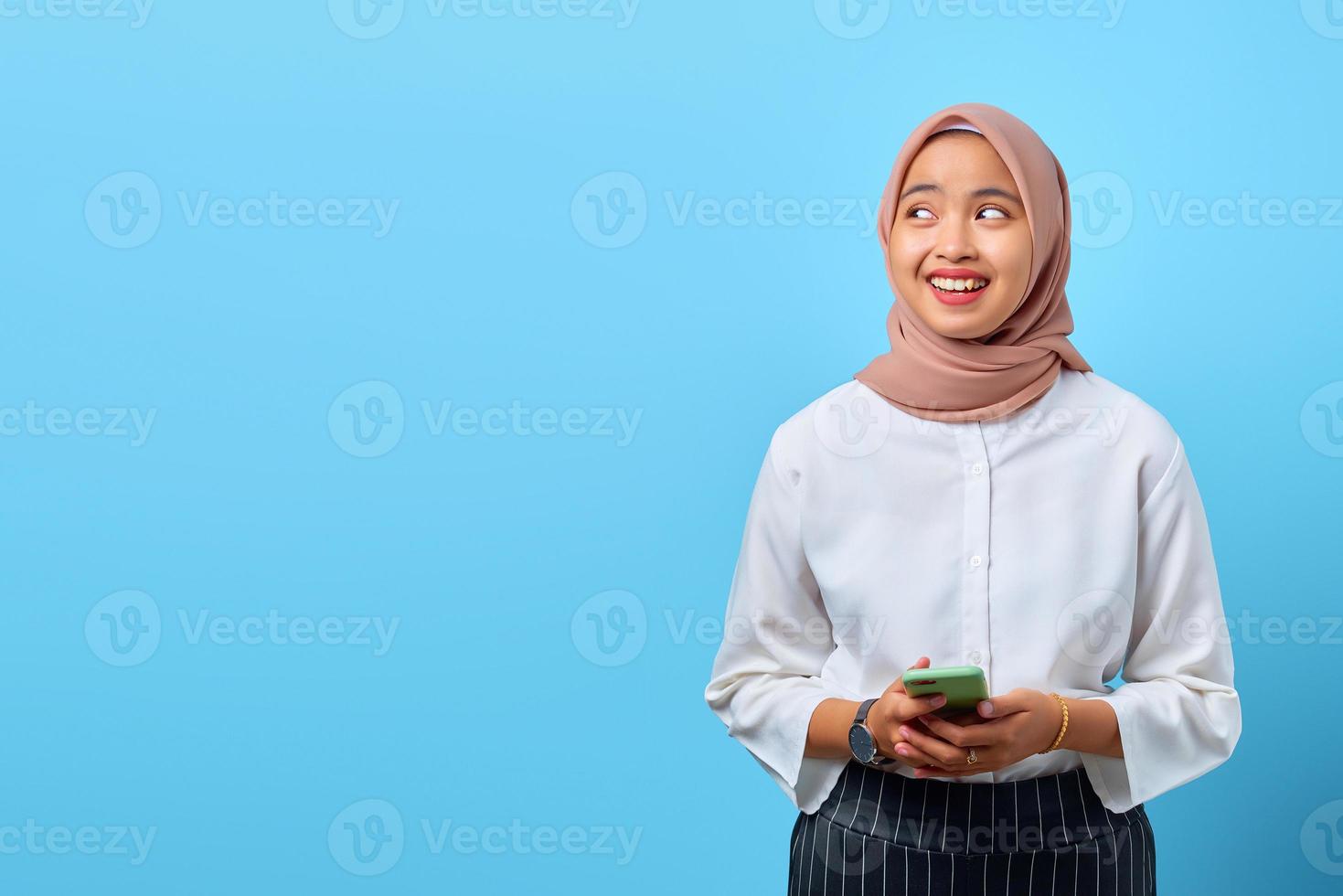 porträtt av leende ung asiatisk kvinna som använder mobiltelefon och ser åt sidan foto