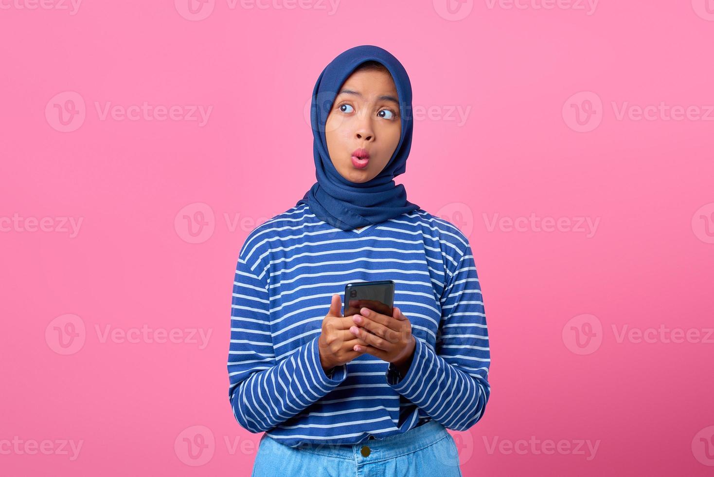 porträtt av chockad ung asiatisk kvinna som håller mobiltelefon och tittar åt sidan foto