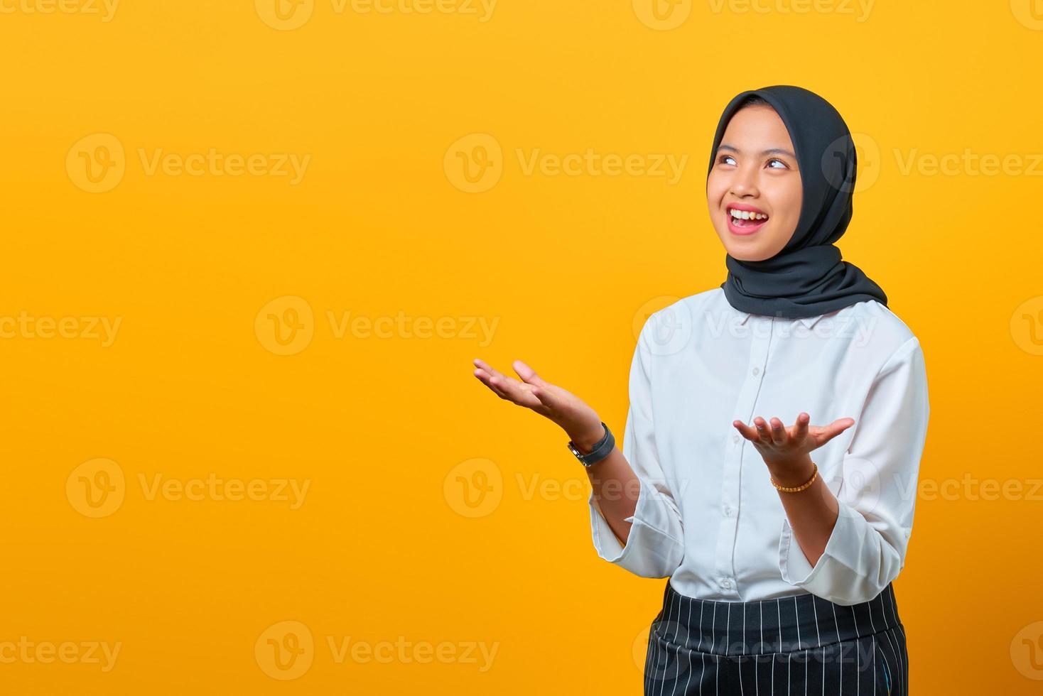 attraktiv ung asiatisk kvinna med skratt ansikte och höjde handen isolerad över gul bakgrund foto