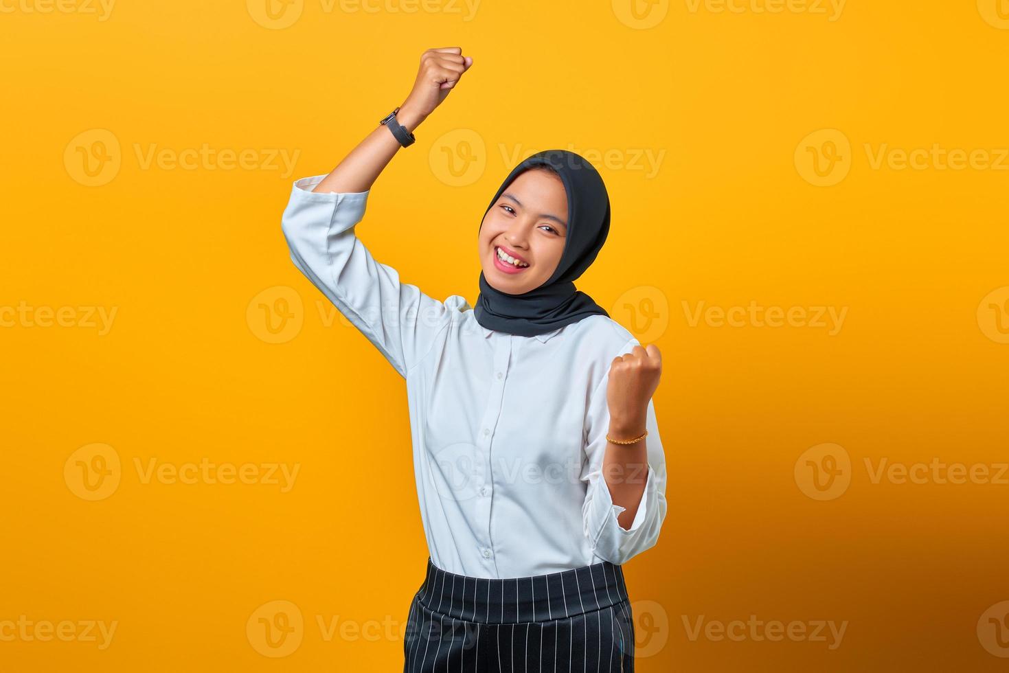 porträtt av upphetsad vacker asiatisk kvinna som jublar över att fira tur på gul bakgrund foto