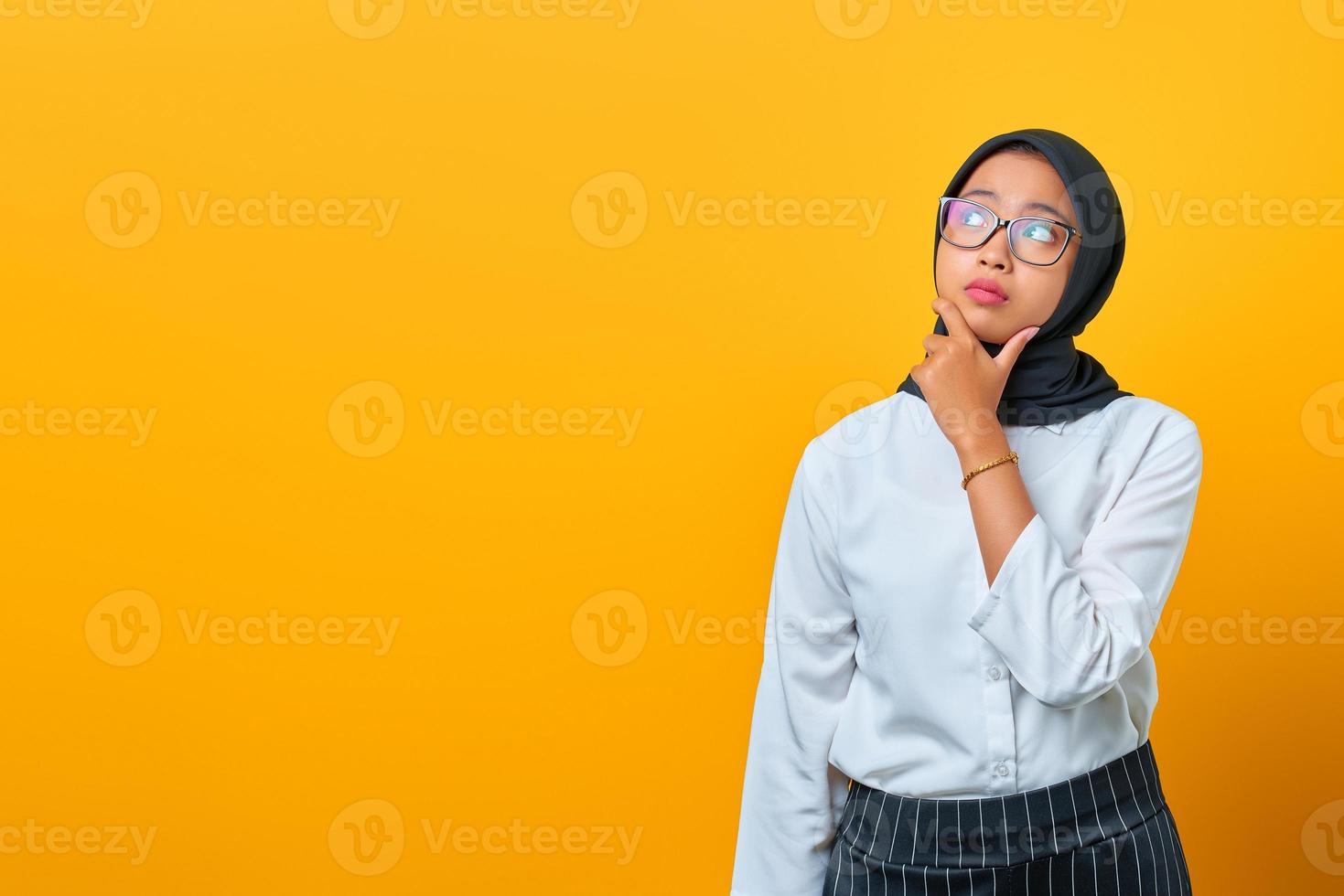 fundersam ung asiatisk kvinna ser seriöst och tänker på en fråga på gul bakgrund foto