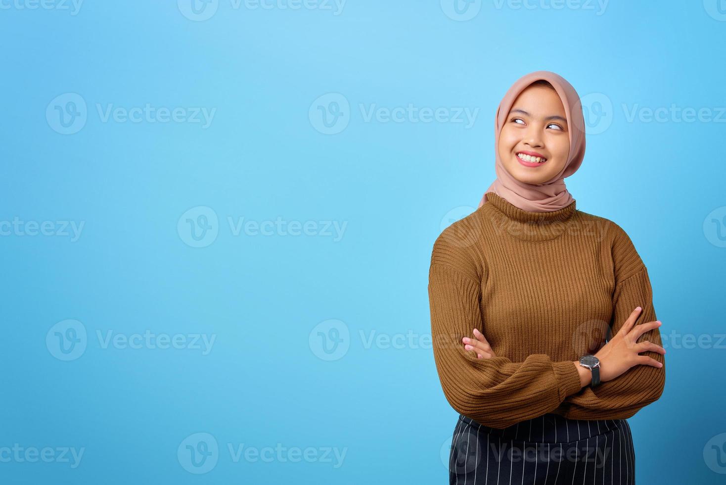 glad ung asiatisk kvinna som korsar armen och ser i sidled på blå bakgrund foto