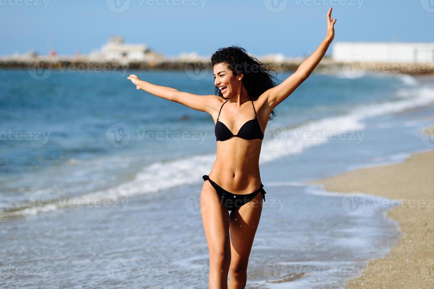 ung arabisk kvinna med vacker kropp i badkläder leende på en tropisk strand. foto