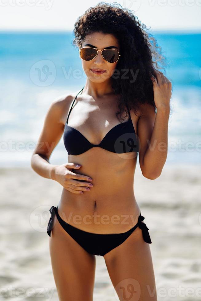arabisk kvinna med vacker kropp i badkläder med flygarsolglasögon på stranden. foto