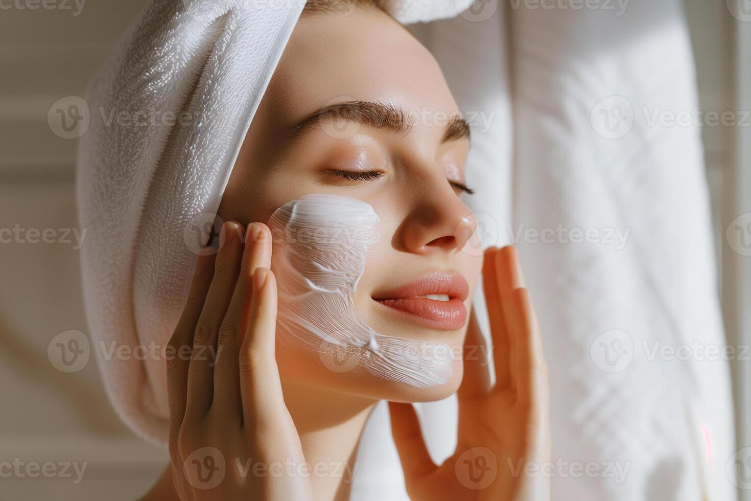 ai genererad skön ung kvinna med vit handduk på henne huvud applicering kosmetisk grädde på ansikte i badrum foto