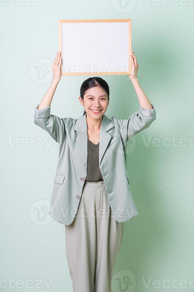 ung asiatisk affärskvinna som håller vit tavla på grön bakgrund foto