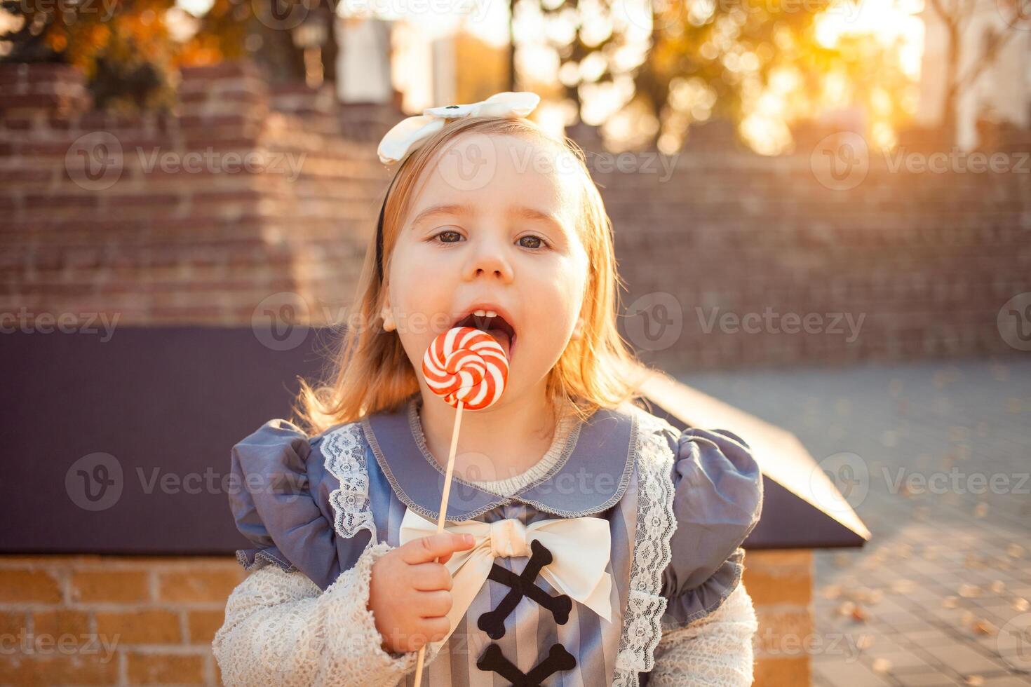 skön liten flicka äter, slickar med tunga utsökt godis, klädd som häxa, utomhus, falla, oktober 31, Lycklig halloween. porträtt rolig. foto