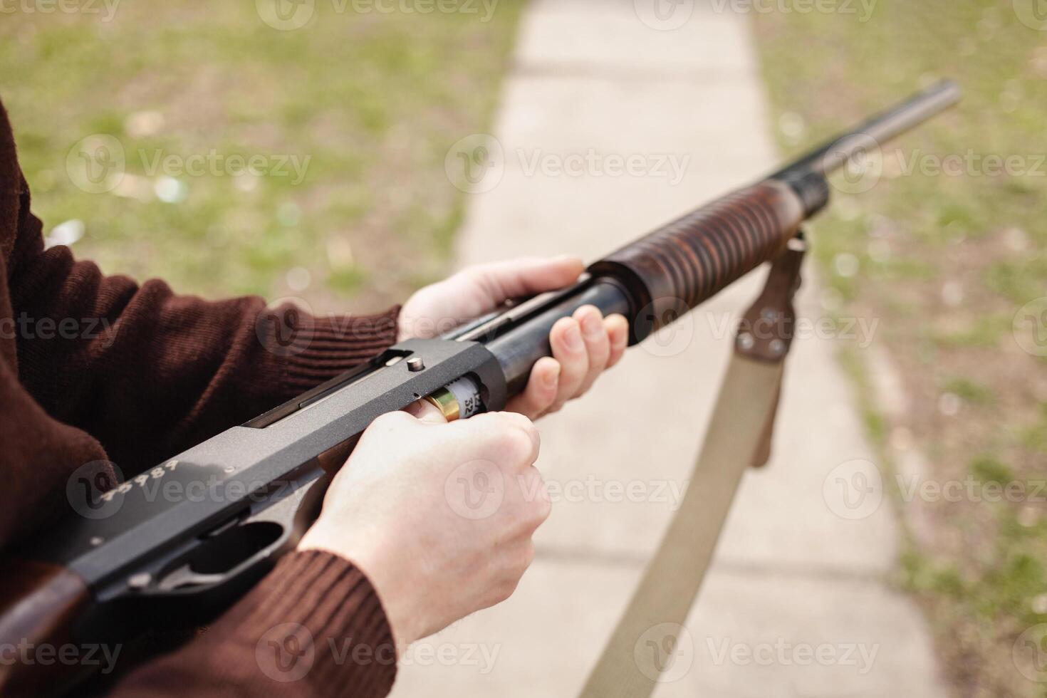 en man kostnader en pumpverkan hagelgevär med en ammunition. 12 kaliber. däck utomhus. en man i hörlurar och glasögon är framställning till skjuta. skjutvapen för sporter skytte, hobby. kopia Plats foto