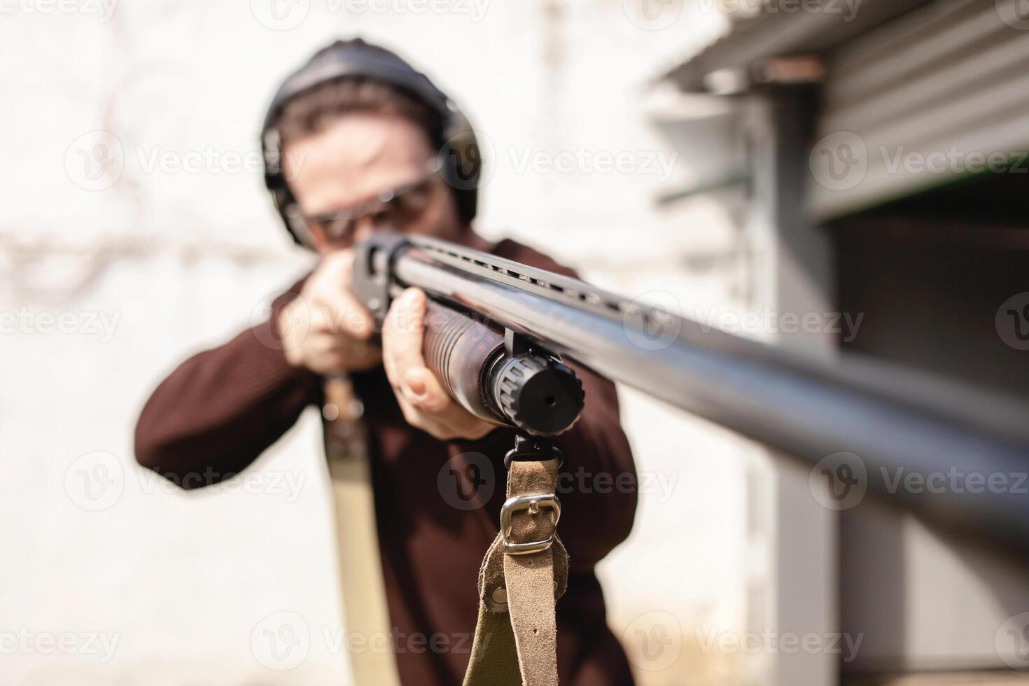 en man med en pompös skjutvapen på en vit bakgrund. en man i skyddande glasögon och hörlurar. däck utomhus. grå hangar. pistol foto