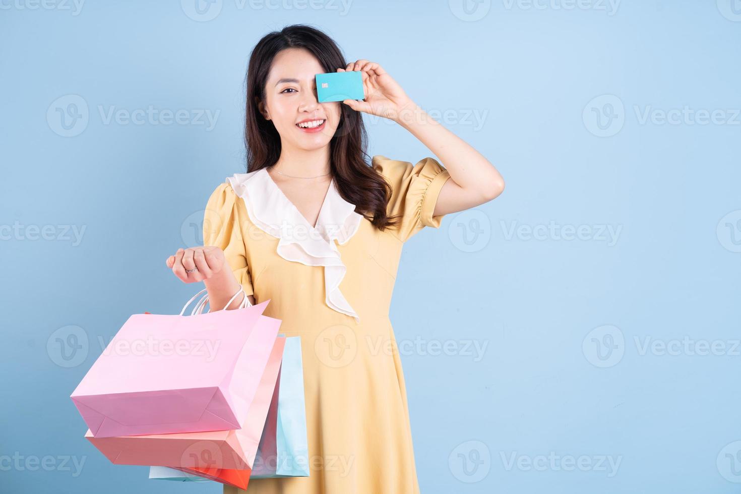 vacker ung asiatisk kvinna med shoppingpåse på blå bakgrund foto