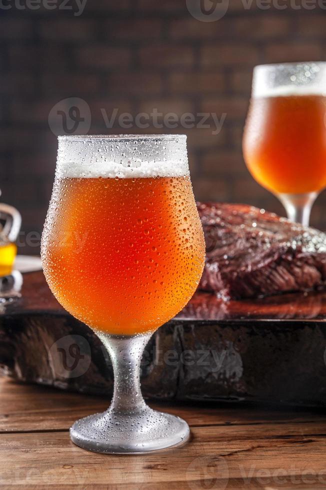 svettiga kalla tulipaglas med öl -fatöl med grillad denverstek på träskärbräda - närbild. foto