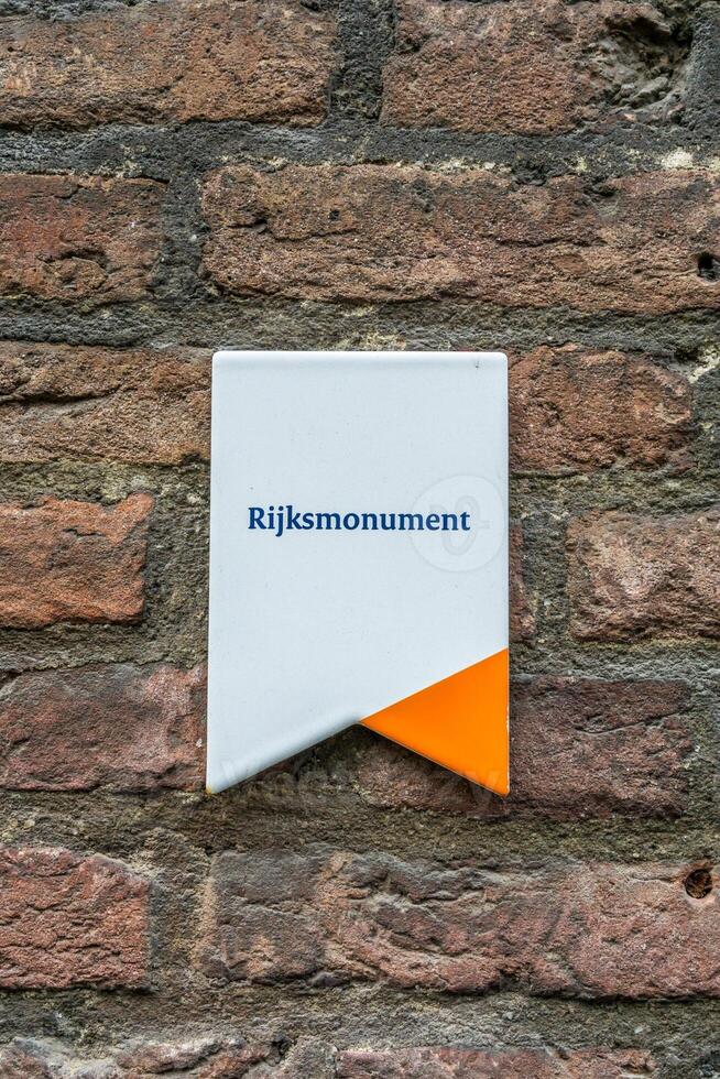 en vit tecken med ett orange markera på en tegel vägg indikerar i dutch den där detta byggnad är nationell monument rijksmonument foto