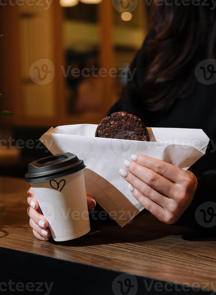 kvinna innehav en råna av kaffe och gröt småkakor i henne händer i kaffe affär foto