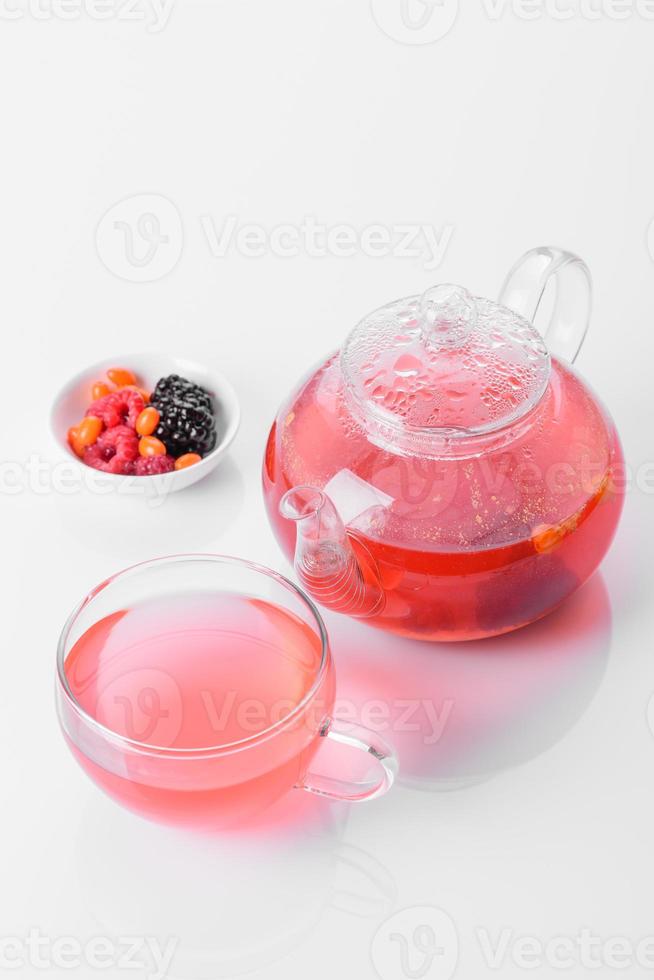 utsökt te av bär och frukter i en vacker glas tekanna på en vit bakgrund med reflektion foto