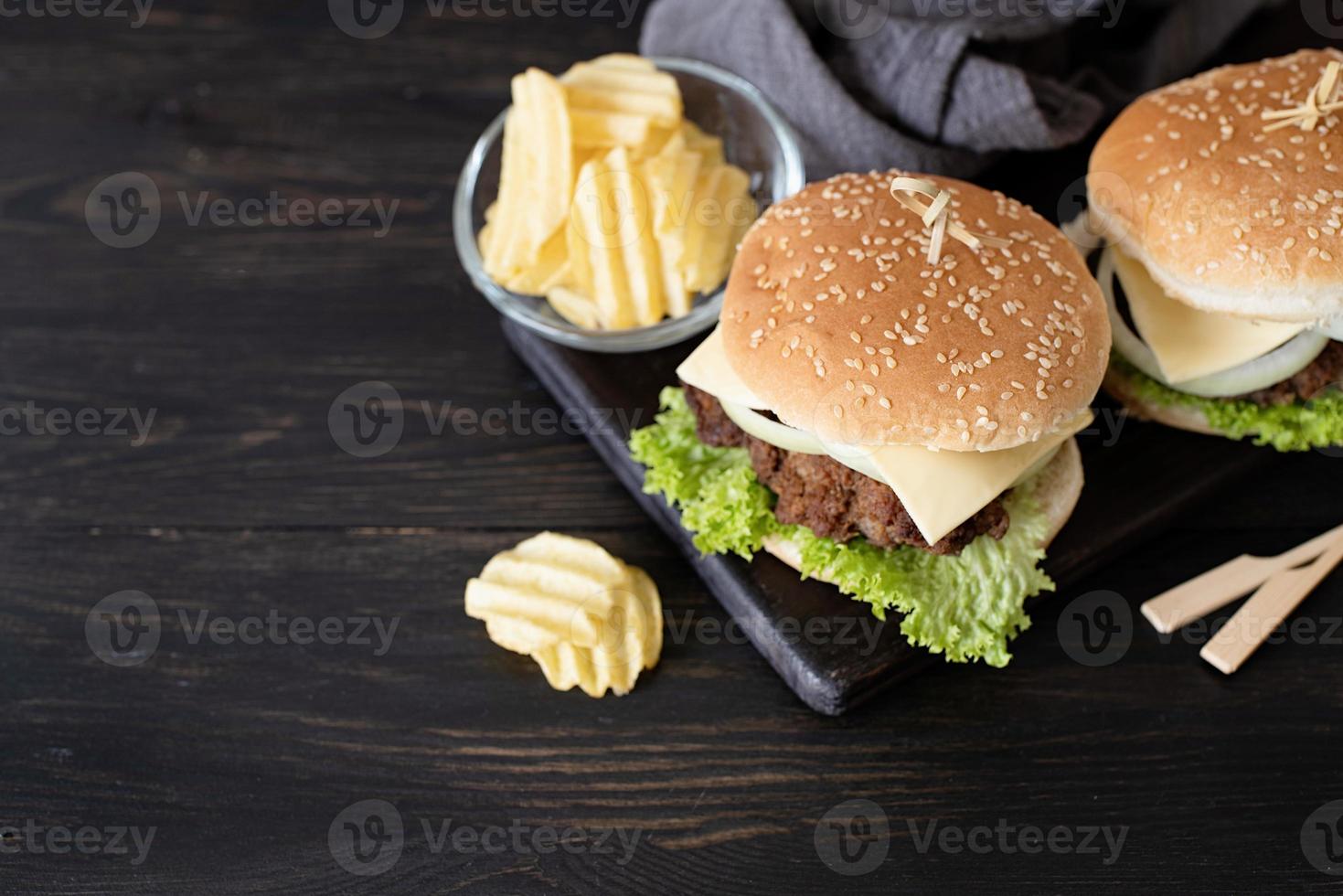 en uppsättning hemlagade läckra hamburgare av nötkött, lök, ost och sallad på en mörk träbakgrund foto