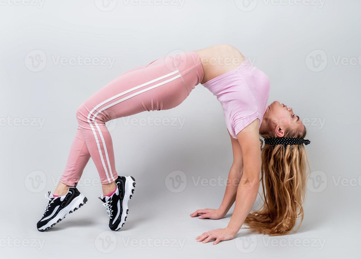 akrobatkvinna iklädd rosa sportkläder som gör övningar i en broställning i studion isolerad på grå bakgrund foto