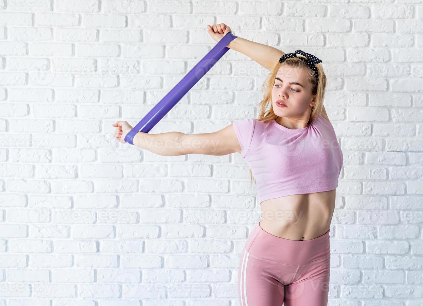 atletisk kvinna gör övningar med hjälp av ett motståndsband hemma på vit tegelväggsbakgrund foto