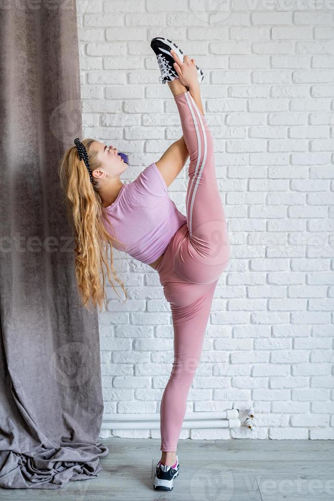 atletisk kvinna bär rosa sportkläder som sträcker sig hemma foto