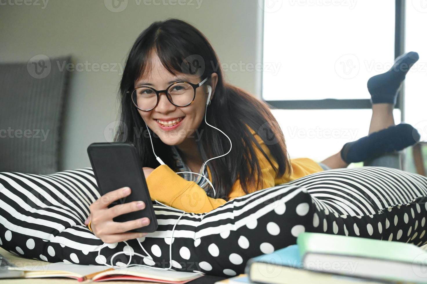 unga kvinnliga studenter bär hörlurar sover på kuddar lyssnar på musik från en smartphone. foto