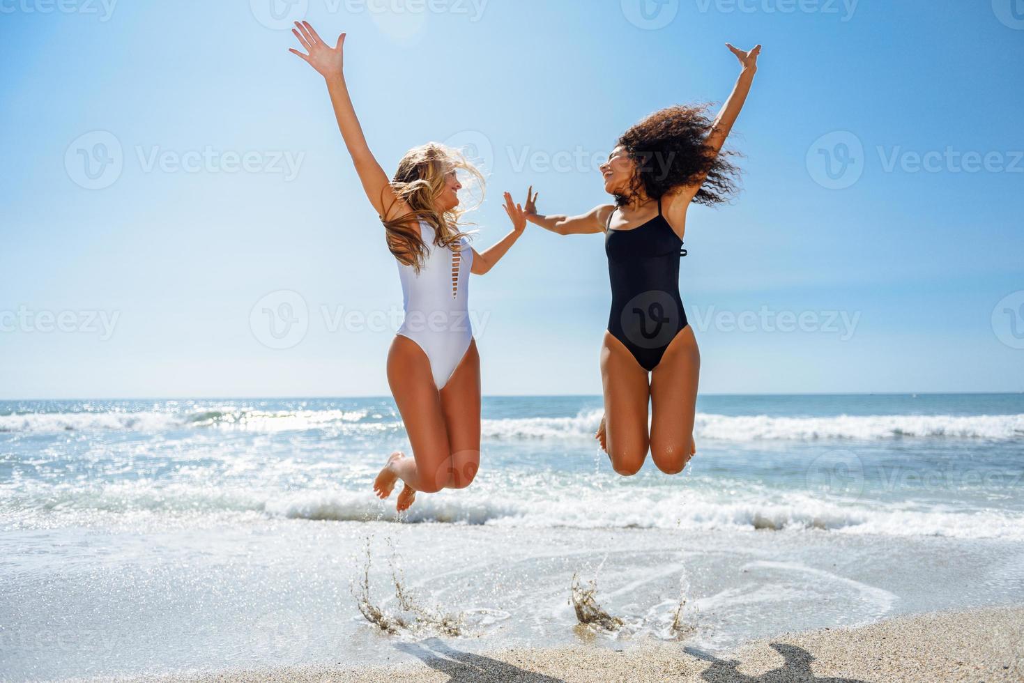 två roliga tjejer i baddräkt som hoppar på en tropisk strand foto