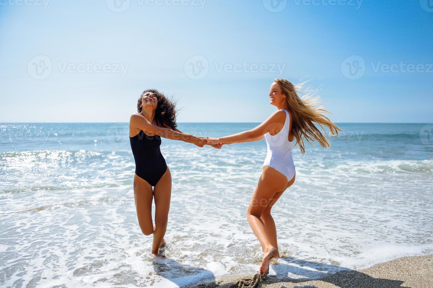 två kvinnor i baddräkt som har kul på stranden foto