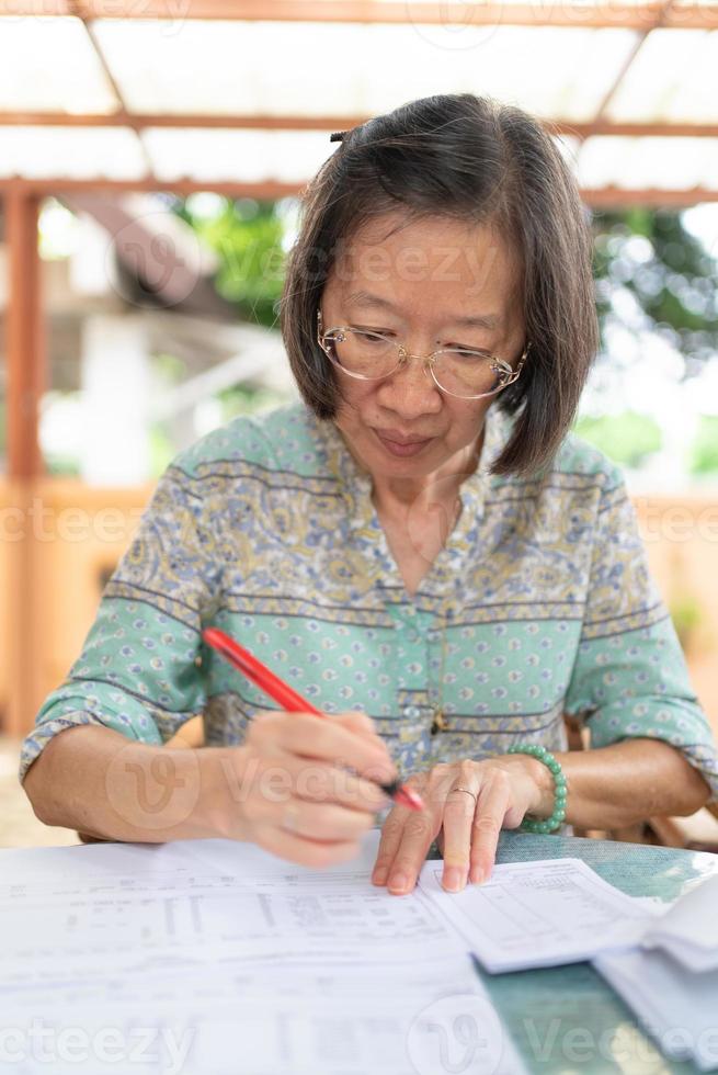 senior asiatisk kvinna beräknar inkomst- och kostnadsbalans på hemterrassen foto