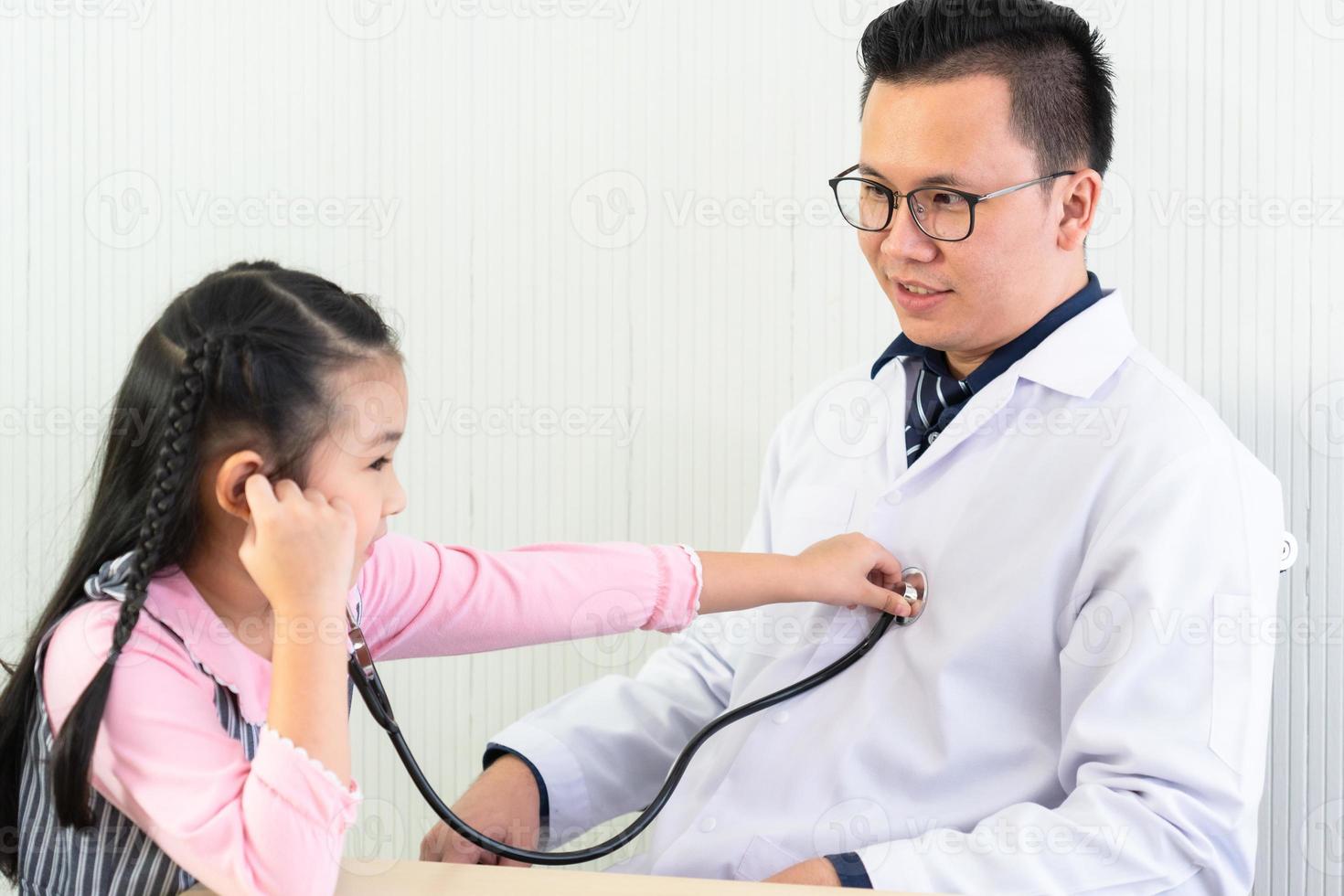 asiatisk läkare lät den unga flickan använda stetoskop för att lyssna på hans hjärta och lunga. sjukvård och barnläkare koncept foto
