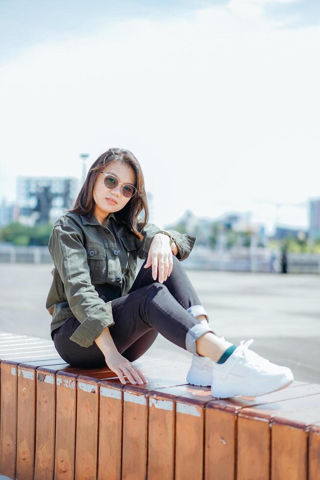 ung skön asiatisk kvinna bär jacka och svart jeans Framställ utomhus foto