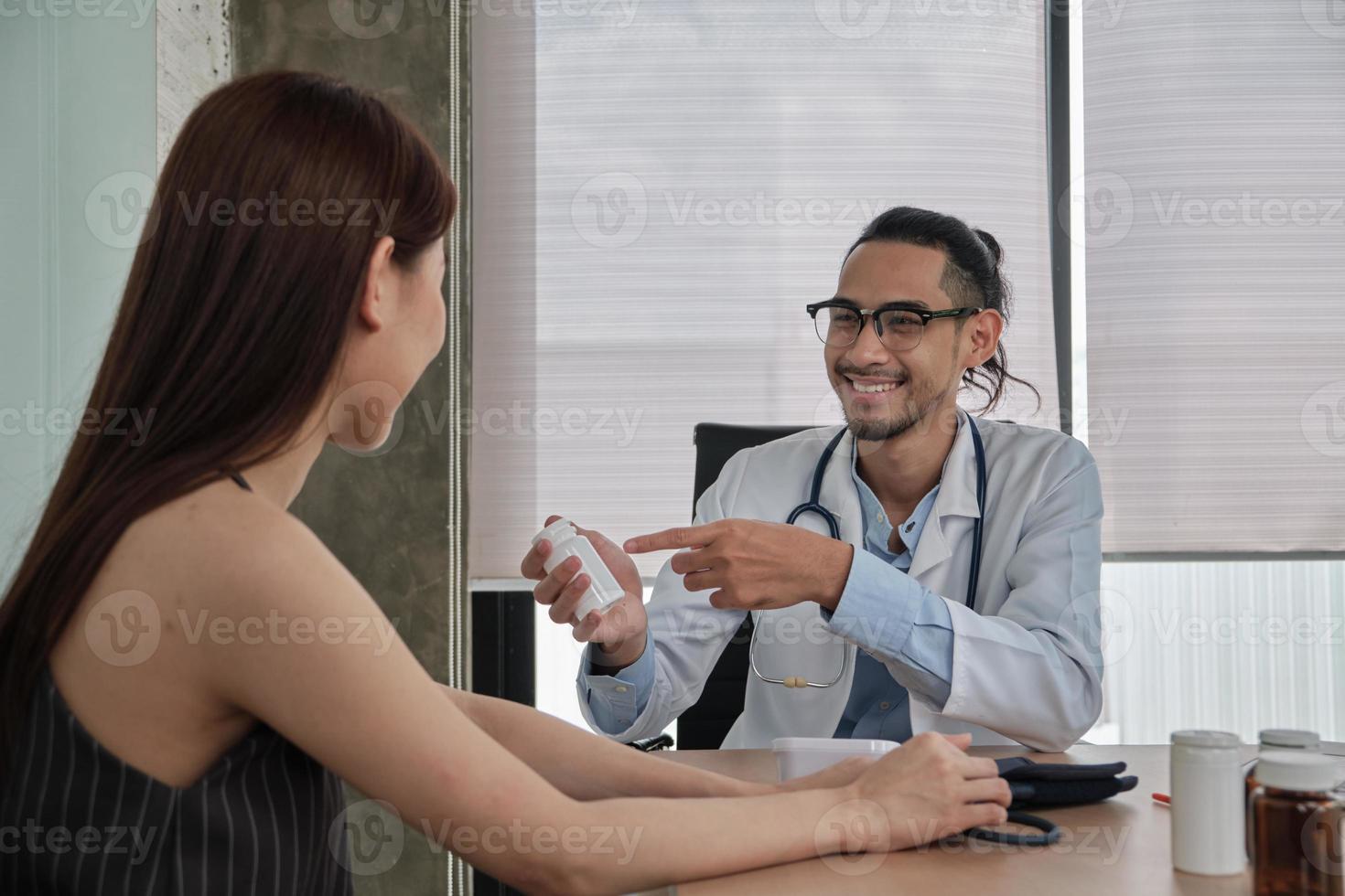 medicinsk behandling och kontroll, ung manlig läkare pratar med ett leende och undersöker en kvinnlig patient med asiatisk etnicitet under ett hälsokonsultationsbesök, råd på en sjukhusklinik. foto