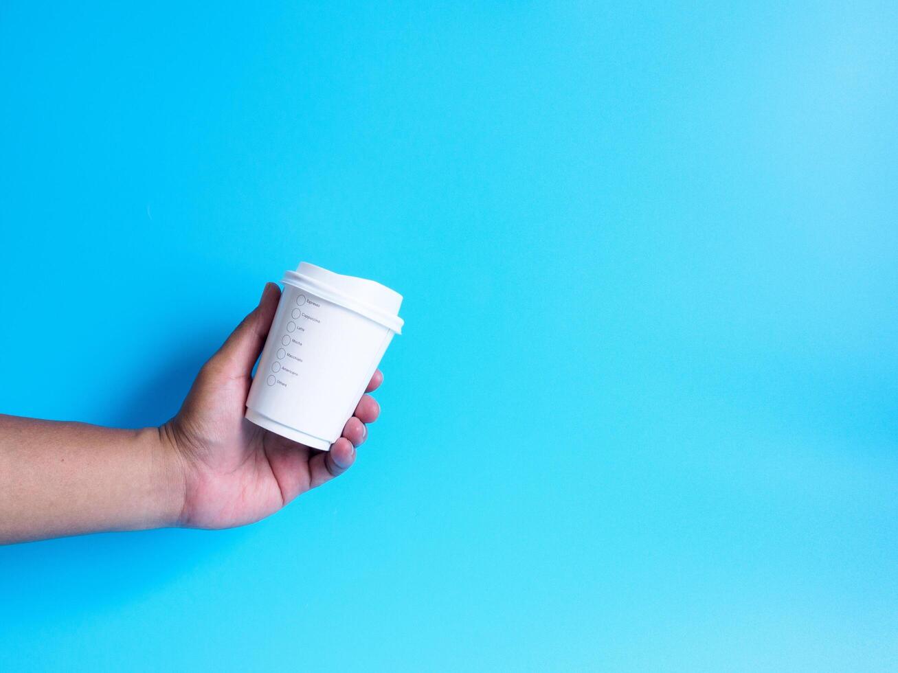 man hand innehav en vit kaffe kopp fylld med varm svart kaffe americano Nej socker Nej mjölk, redo till dryck, uppfriskande. arom vaken färsk till arbete placerad på en blå isolerat bakgrund foto