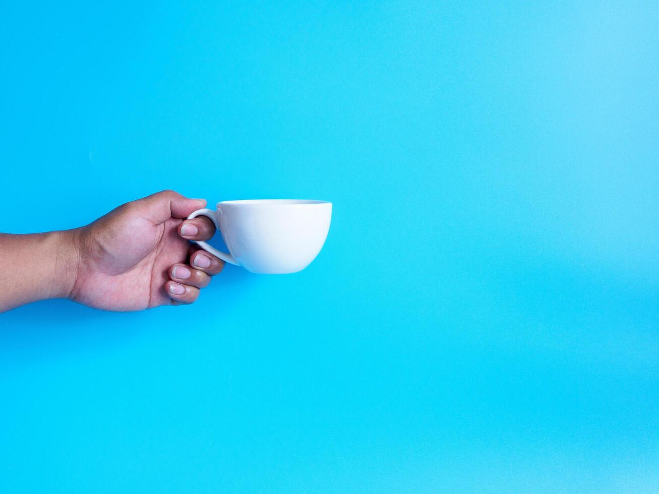 man hand innehav en vit kaffe kopp fylld med varm svart kaffe americano Nej socker Nej mjölk, redo till dryck, uppfriskande. arom vaken färsk till arbete placerad på en blå isolerat bakgrund foto