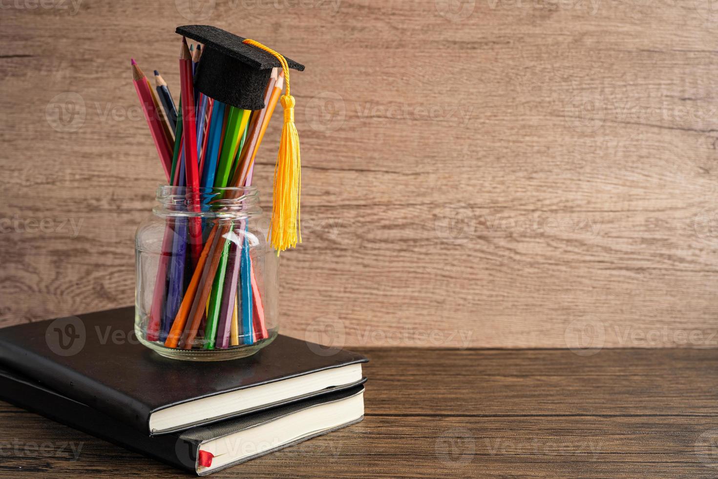 examen hatt med färgglada pennor på bok med kopia utrymme, lärande universitet utbildning koncept. foto