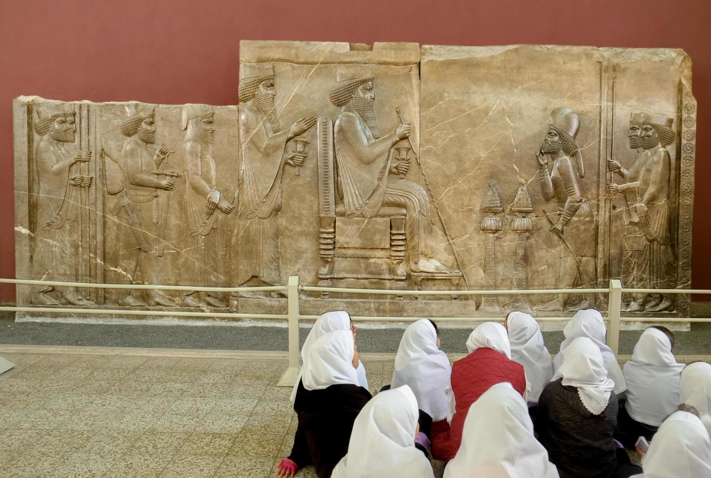 tehran, iran, 2016 - skolflickor i vit hijab som deltar i historielektion framför persepolis bas -relief av kung darius på nationalmuseet. foto