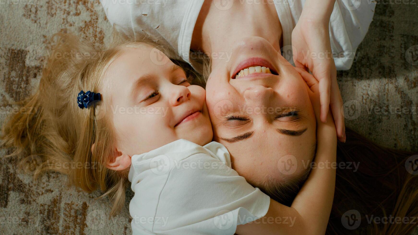 söt öm antogs liten unge förskola flicka kramas kel mor huvud topp se. barn dotter med mamma två ansikten omfamning liggande ner på Hem talande leende med ögon stängd anbud ögonblick foto