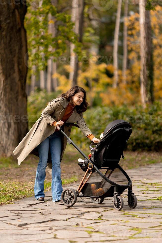 ung kvinna med söt bebis flicka i bebis sittvagn på de höst parkera foto