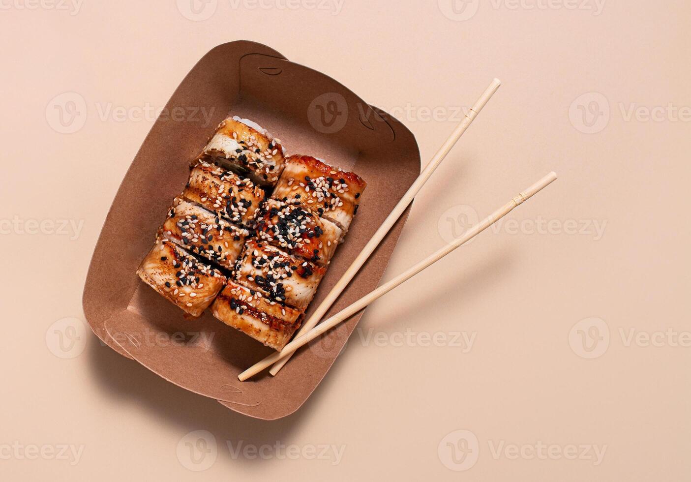 asiatisk sushi. sushi med ål, sås och sesam i en papper behållare på en ljus bakgrund. mat leverans. sida se. kopia Plats. foto