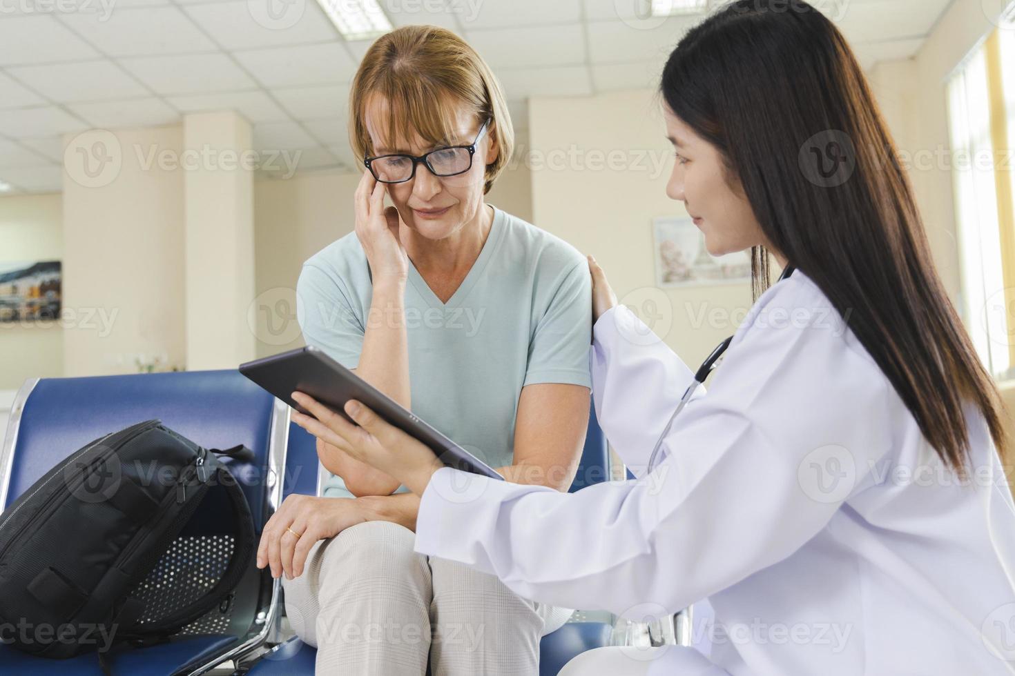 kvinnlig läkare ger råd till den gamla kvinnan patienten genom en tablett på sjukhuset. foto