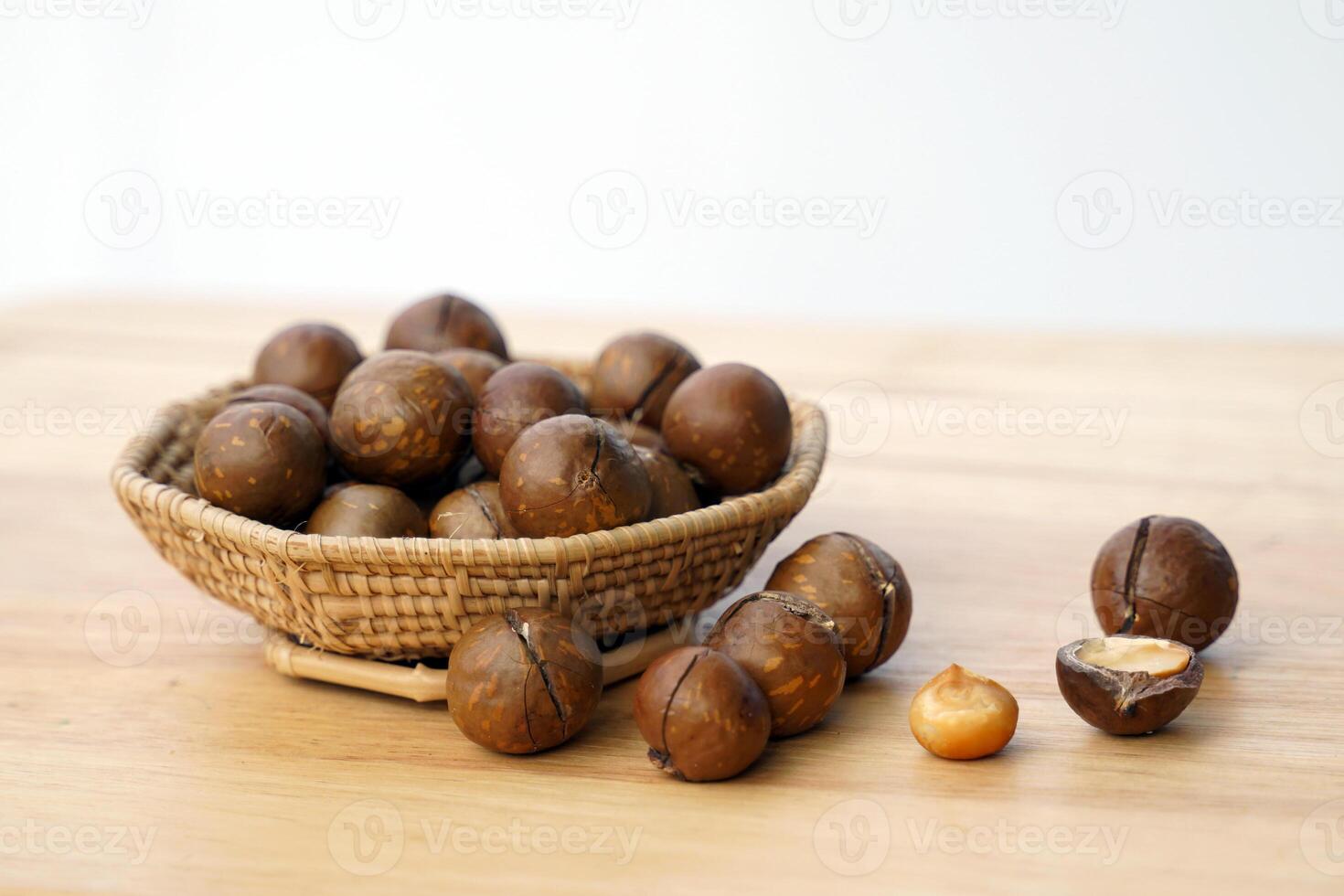sida se av en korg av rostad macadamia frön på en trä- tabell med macadamia nötter spridning ut. de frön ha smak. och en doftande textur rik i många näringsämnen. foto