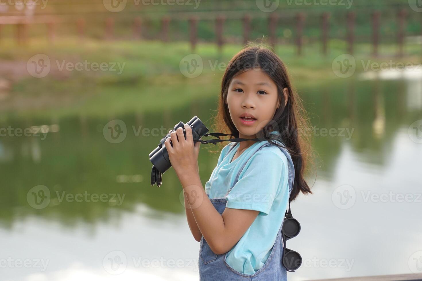 asiatisk flicka användningar kikare till observera de natur, fåglar, och djur av de nationell parkera medan camping med henne familj. med de begrepp av inlärning utanför de klassrum natur studie, utforskning. foto