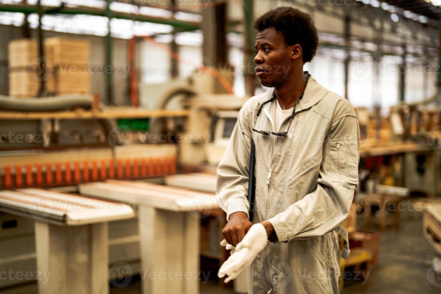 afrikansk man arbetare teknik stående med förtroende med arbetssätt svit klänning och hand handske i främre maskin. begrepp av smart industri arbetstagare fungerar. trä fabrik producera trä gom. foto