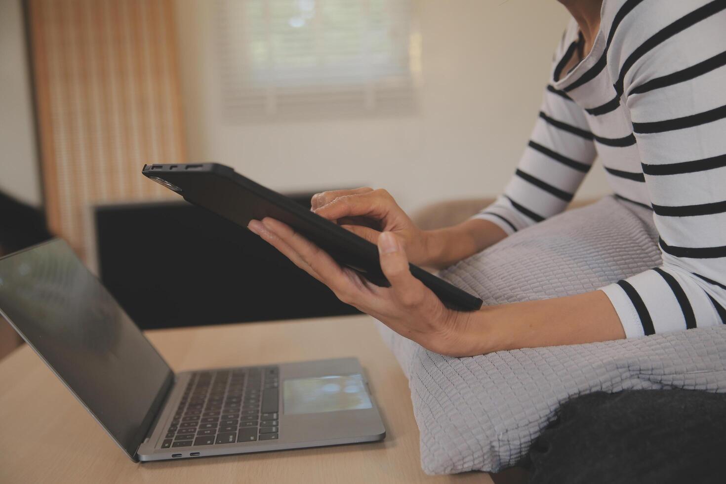 ung attraktiv asiatisk kvinna vilar använder sig av bläddring läsplatta dator på soffa på Hem, Lycklig flicka Sammanträde på soffa koppla av läsning digital grej med upphetsad, kommunikation och livsstil begrepp. foto