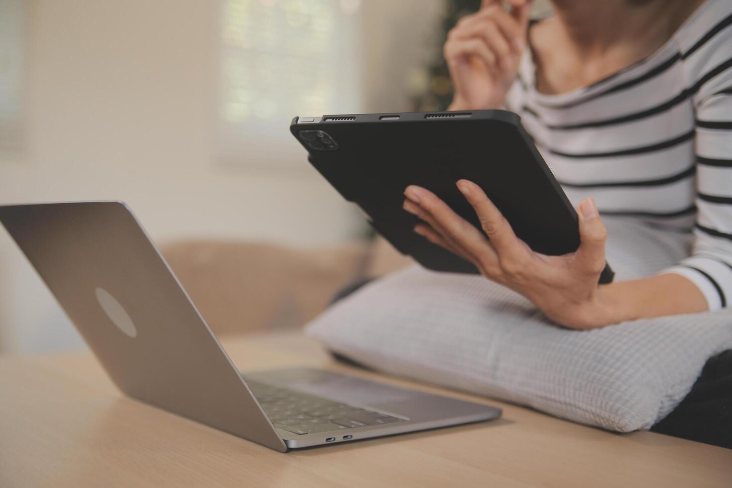 ung attraktiv asiatisk kvinna vilar använder sig av bläddring läsplatta dator på soffa på Hem, Lycklig flicka Sammanträde på soffa koppla av läsning digital grej med upphetsad, kommunikation och livsstil begrepp. foto