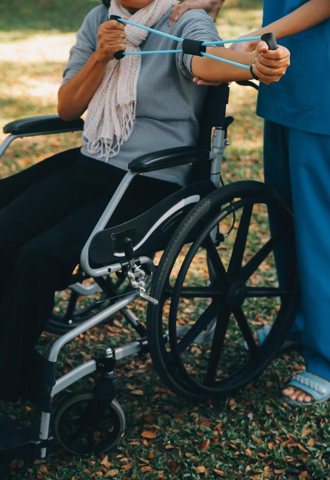 ung sjuksköterska eller fysioterapeut i scrubs portion en Lycklig pensionerad gammal kvinna do kondition övningar med ljus vikt hantlar på Hem. begrepp av fysioterapi för seniors foto