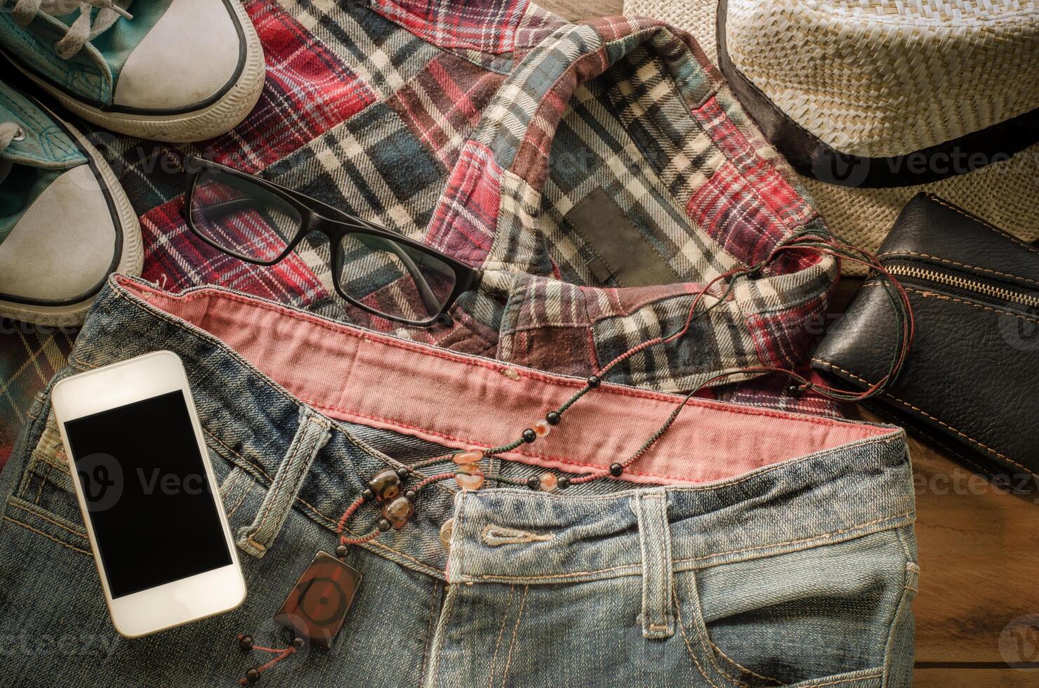tillbehör smart telefon jeans skor, plånbok, jeans, hattar skjorta på en trä- golv för resa foto