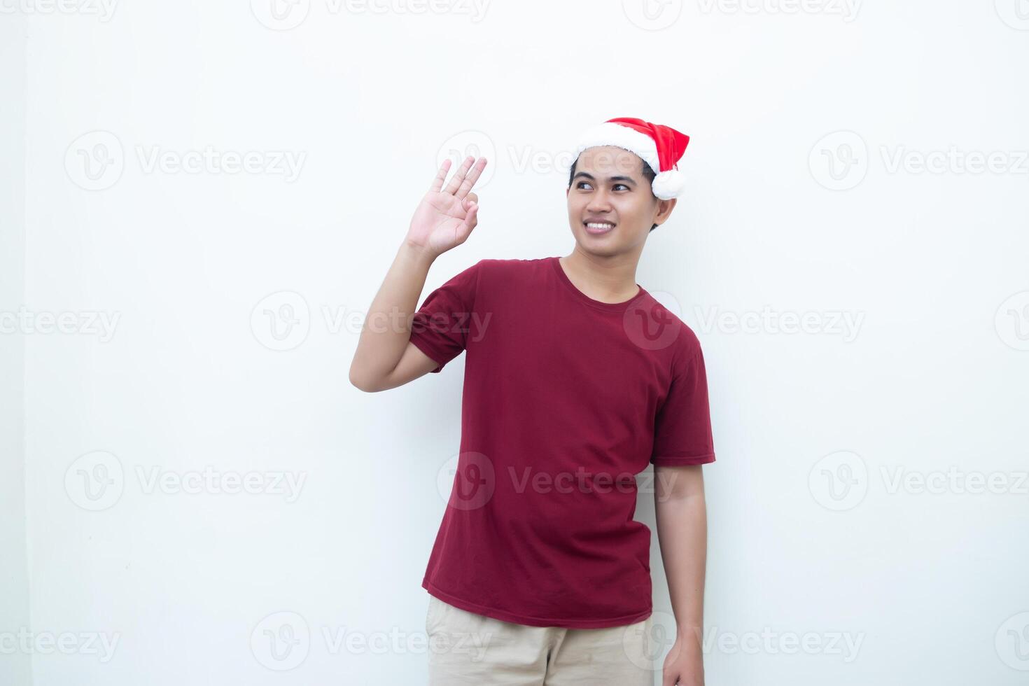 ung asiatisk man bär en santa claus hatt med en hand framställning de ok gest isolerat förbi en vit bakgrund för visuell kommunikation foto